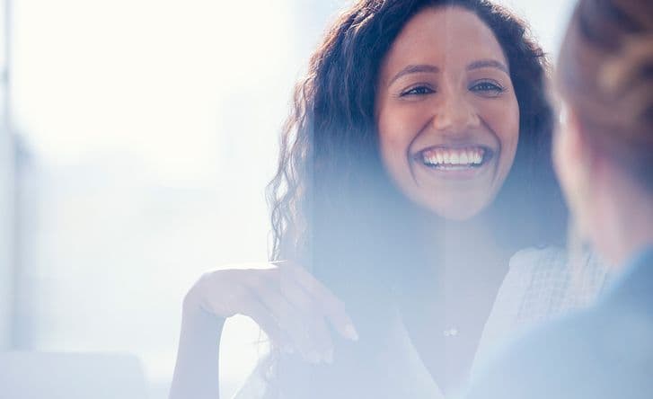 A close up of a woman's face, she's talking to a female colleague and smiling.