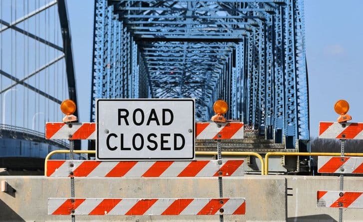 A photo of a bridge with a large blockade across it and a sign that says 'road closed'.