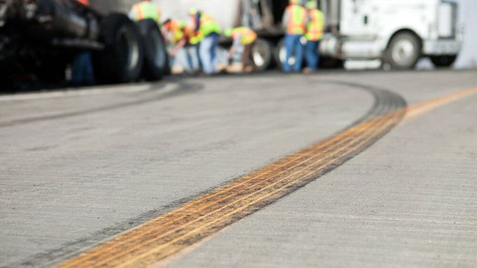 A close up shot of black tyre marks on grey concrete, with white trucks and people in high vis in the background.