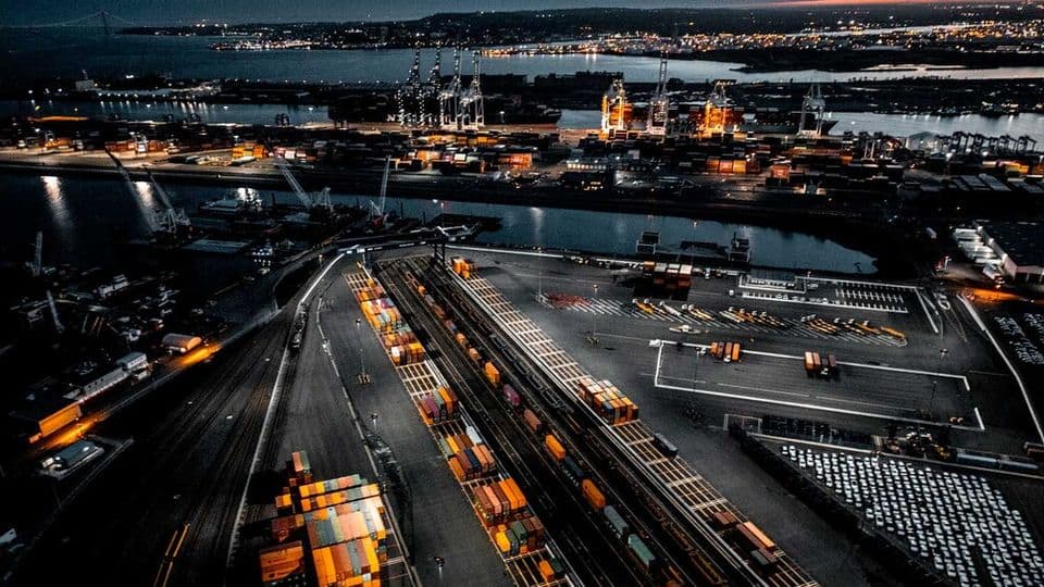 An over head shot of a ship yard and docks full of containers in different colours. The photo is taken at night and the port is lit up.