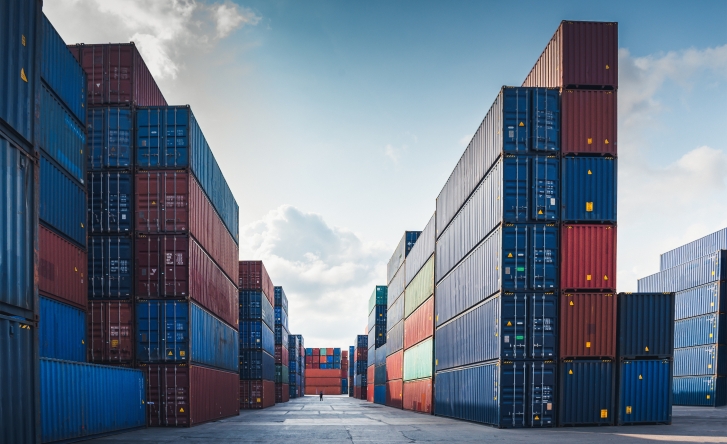 A photo of a ship yard containing piles of shipping containers which are stacked neatly. They are blue, red, green and orange.