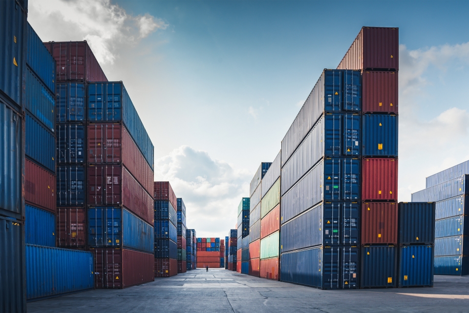 A photo of a ship yard containing piles of shipping containers which are stacked neatly. They are blue, red, green and orange.