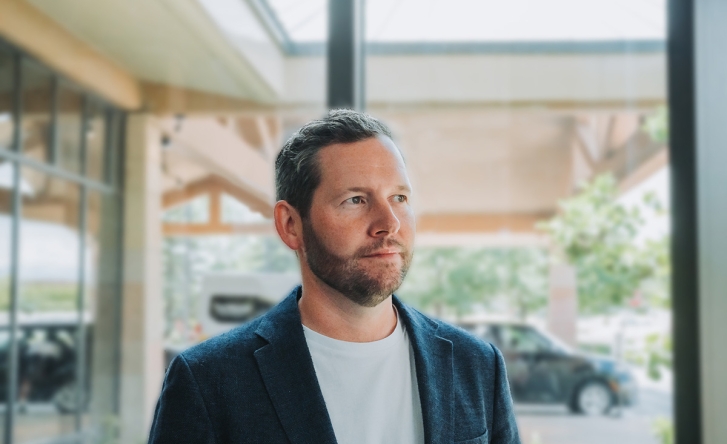 A headshot of Johnny McCord, wearing a navy blazer and white tshirt. Johnny is smiling slightly and looking off to the right of the camera.