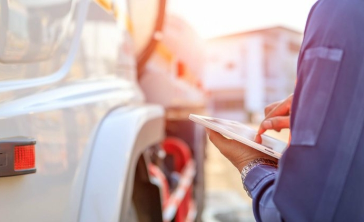 A closeup taken over someone's shoulder of a hand using a tablet at work, with a truck on the left.