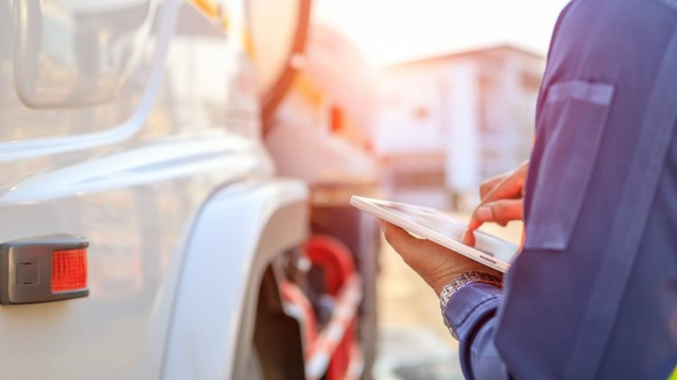 A closeup taken over someone's shoulder of a hand using a tablet at work, with a truck on the left.