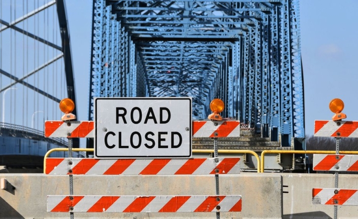 A photo of a bridge with a large blockade across it and a sign that says 'road closed'.