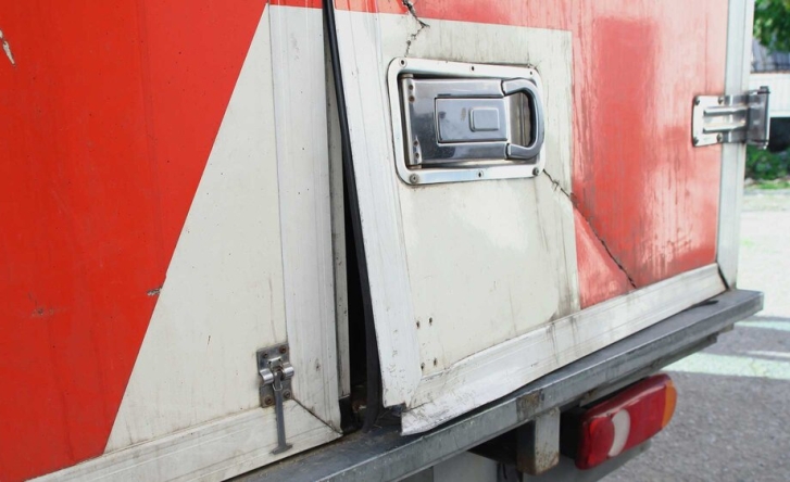 A photo showing the corner of a red and white cargo truck where it's clear that entry has been forced - the door is bent and a crack runs through the cover.