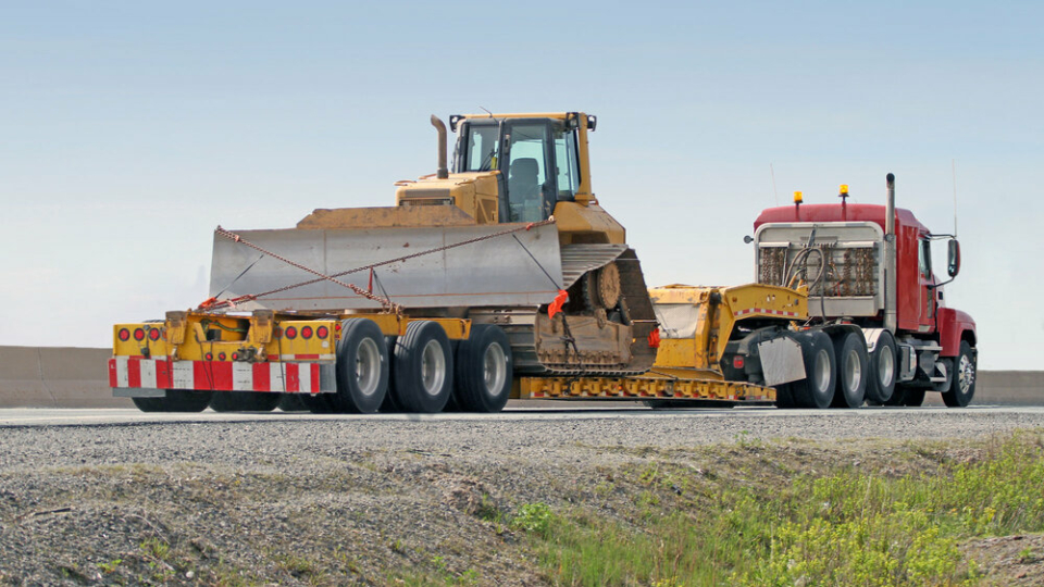 An image of a bulldozer on top of a cargo truck, being towed away