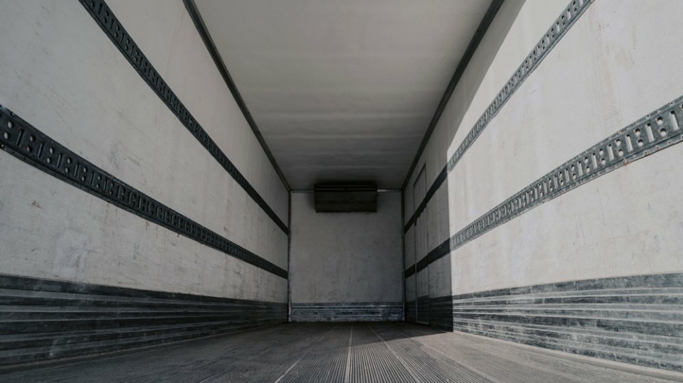 A photo of the inside of an empty cargo truck, with white walls and a black floor.