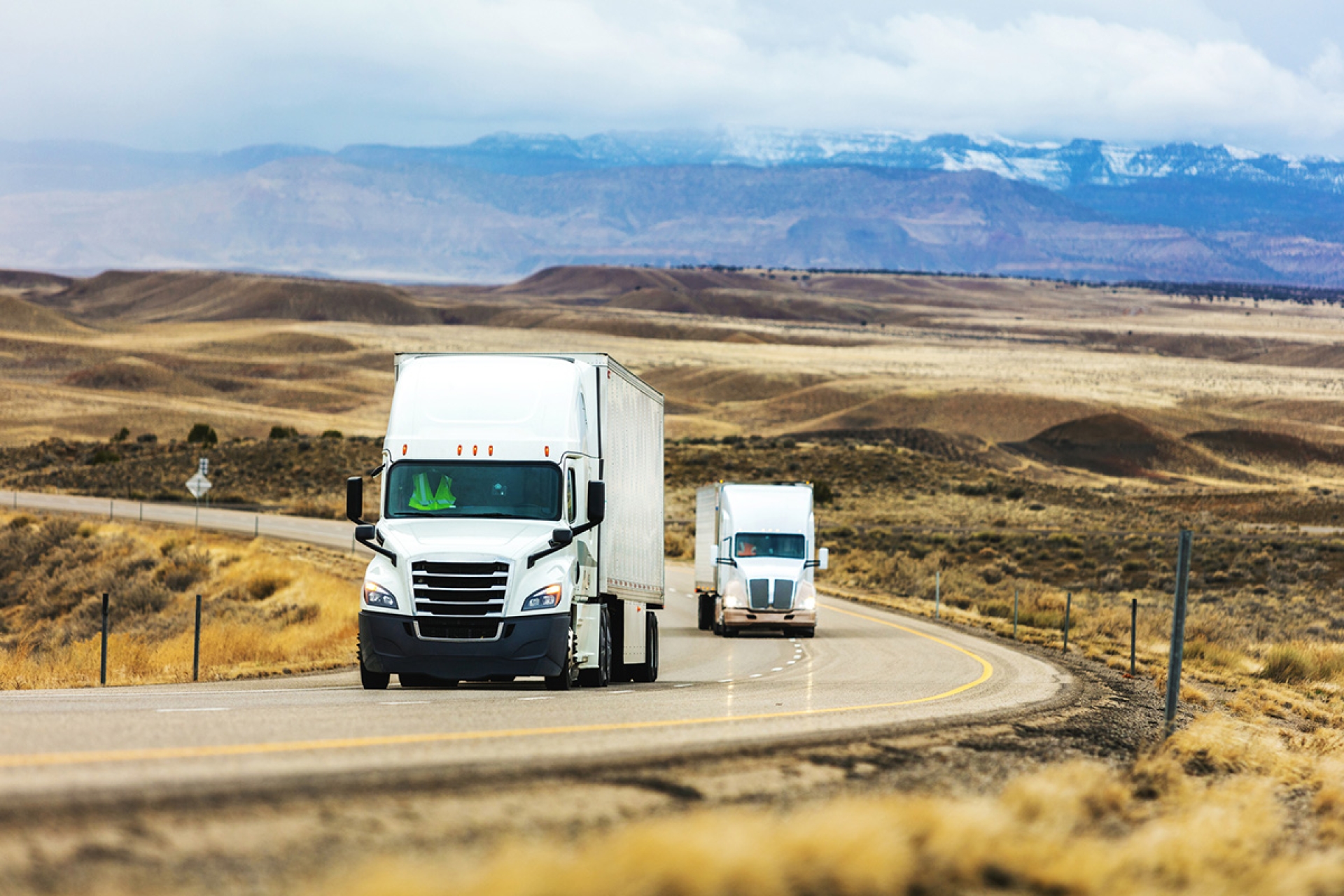 Two trucks are driving along a highway with mountains in the background