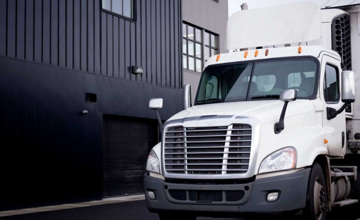 A white cargo truck parked next to a black and grey building on the left.