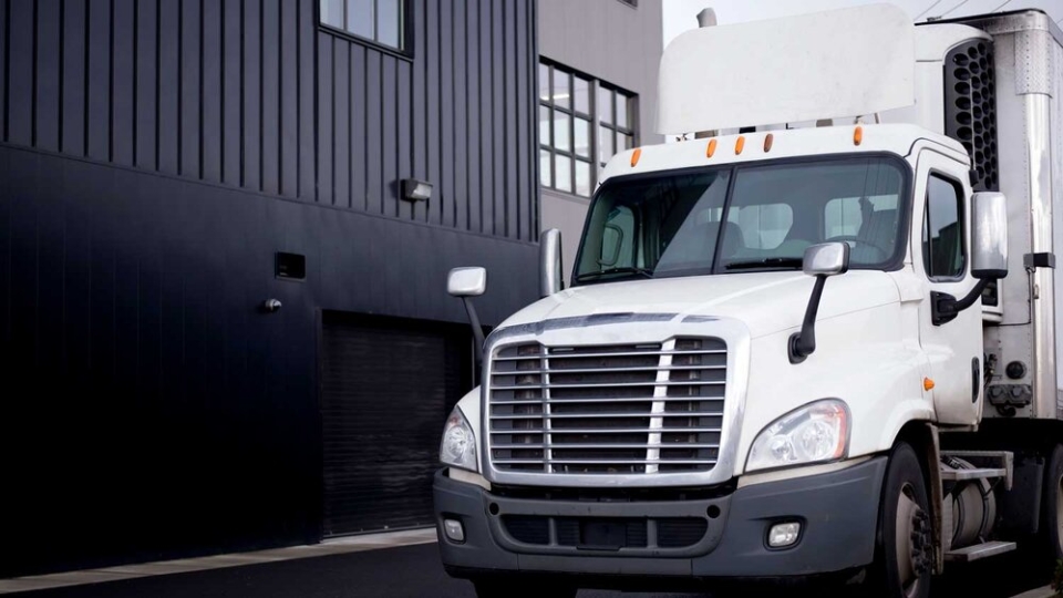 A white cargo truck parked next to a black and grey building on the left.