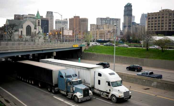 An image of a highway in a city with two trucks in the foreground, one blue on white.