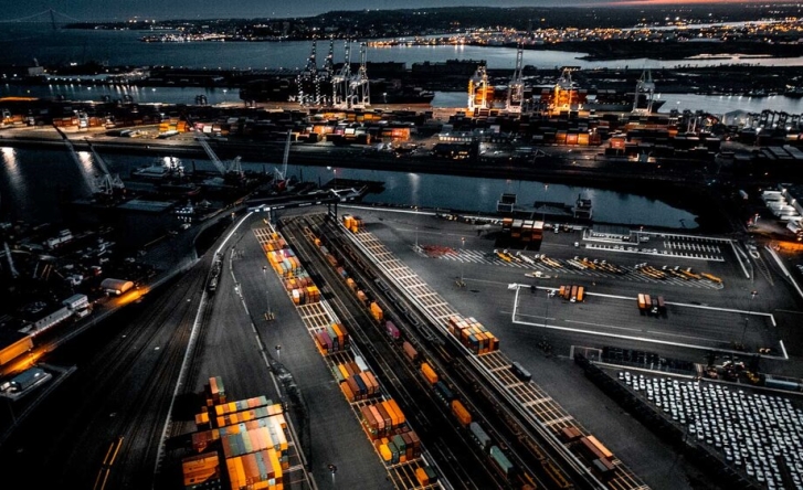 An over head shot of a ship yard and docks full of containers in different colours. The photo is taken at night and the port is lit up.
